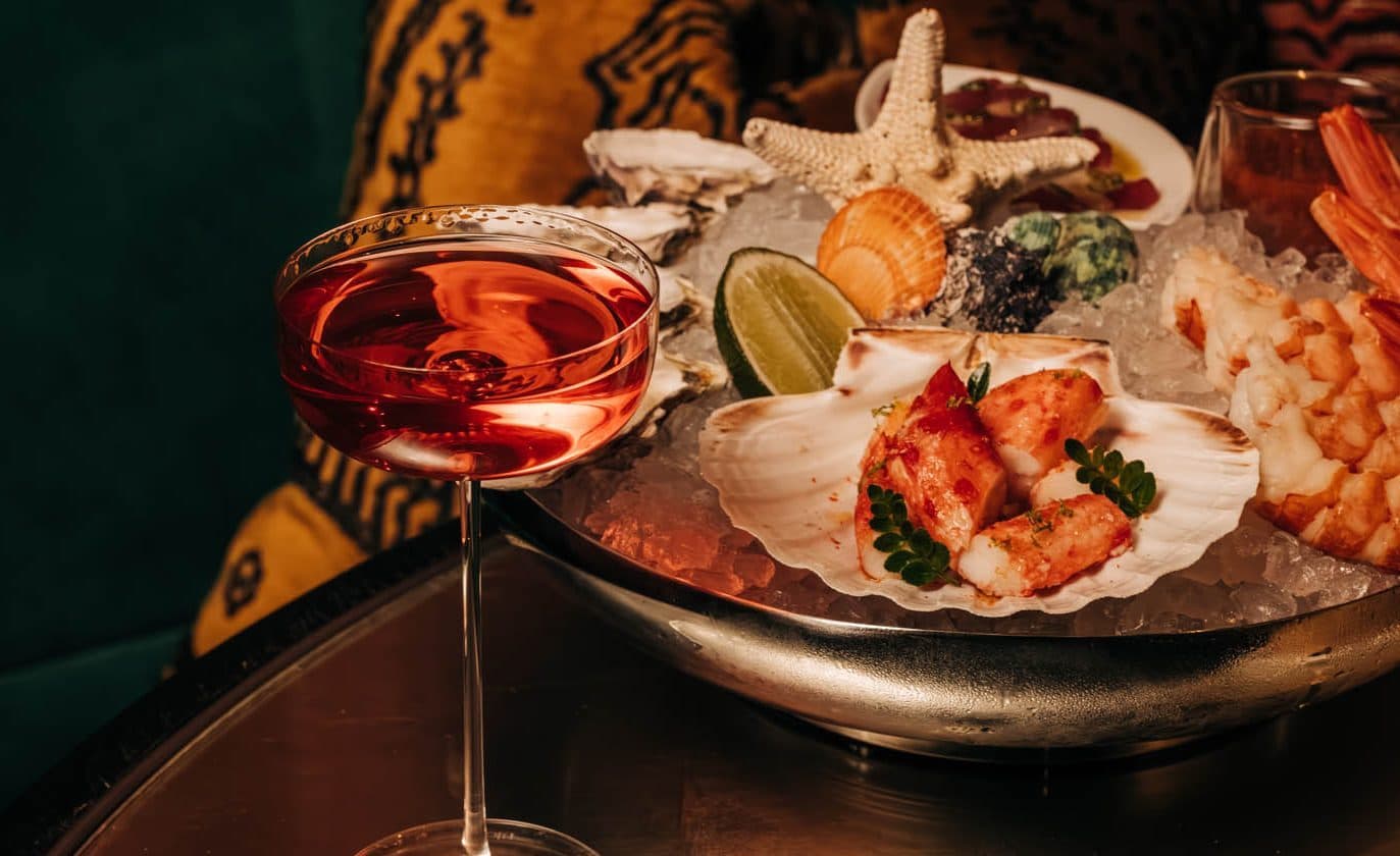 cocktail in a coupe glass on a table with a raw spread behind it.